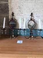 Pair of brass colored wall candle sconces, each with oval mirror and two candle holders with clear crystal prism decorations.