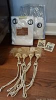 Packaged white solid outdoor drapes with metal grommets, and 4 cream-colored fringed rope tie backs with holders laid out in front.