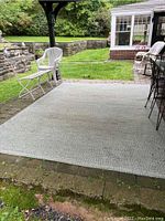 Outdoor patio with white chairs showing the large woven outdoor rug beneath them in a neutral blue-green-cream hue.