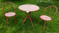Full view of red metal patio set including round table and 2 chairs on grass, showing layout and design