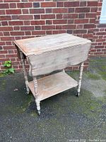 Full view of the wooden rolling tea cart outdoors showing two drop-leaf sides in lowered position and lower shelf with visible wear
