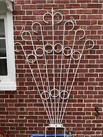 Full view of the white metal trellis showing its fan-shaped design installed against a brick wall.