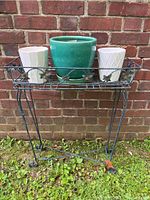 Full view of wire plant stand holding three pots against brick wall.