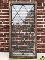 Front view of one wood framed decorative glass window with diamond leaded solder pattern against brick background, showing weathered frame and clear glass.