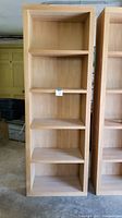Front view of one wooden bookcase showing five fixed shelves and light wood finish.