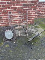 Photo showing wrought iron foldable shelf, magazine rack, and framed mirror placed on the ground against a brick wall.