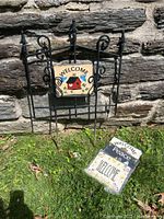 Wrought iron sign holder stuck in grass with one slate sign attached and 4 other slates laid on ground around it