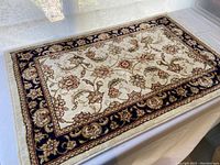 Area rug showing full rug with floral and vine pattern, cream center, and navy blue border.
