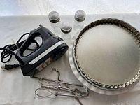 Photo of black KitchenAid handheld blender with attached cord, three metal mixing attachments, three spice jars, two quiche plates and one pie plate.