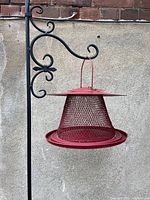 Red cardinal bird feeder hanging from black metal post mounted on wall