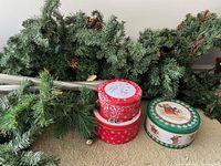 Photo of three artificial garland strings laid out and three Christmas-themed cookie tins (red with reindeer design, green with bear on sled)