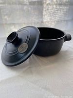 Side angle of charcoal ceramic round Dutch oven with lid propped open showing interior and Emile Henry logo on lid knob.