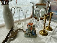 Overview of lot items including glass candle pillars, flower vases, brass candleholders, clocks, ceramic figurine, glass paperweight, and decorative metal shoe.
