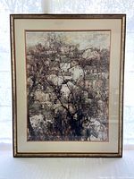 Framed picture showing houses behind trees in muted colors, visible signature M. de Guillaud in top right.