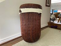 Photo of the full laundry basket showing woven wicker construction and the fabric liner tied to the top edge, placed on carpet next to wooden flooring.