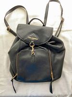Front view of small black leather Karl Lagerfeld backpack showing flap, front zippered pocket, and straps.