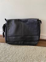 Front view of the black leather Kenneth Cole messenger bag, showing the flap and stitching detail.