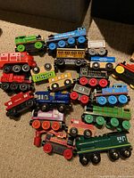 Multiple colorful wooden toy trains arranged on carpet showing various designs and colors.