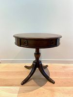 Full front view of the round hardwood pedestal table showing the single drawer and curved legs.