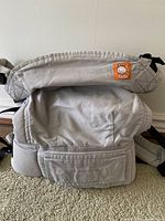 Gray Tula baby carrier front view showing main body, waistband with pocket, and logo patch