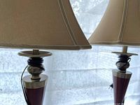 Close view of two table lamps with wood and silver bases topped with beige fabric shades, showing screw top shade attachment mechanism that sits rather than screws on.