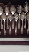 Twelve silver plated souvenir teaspoons from 1939 NY World's Fair with visible tarnish and light scratches, arranged in a display case.