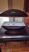 Front view of the AeroGarden showing the light panel labeled AeroGarden, 7 plant holes, and base with control buttons.
