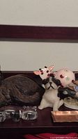 Shelf with cast iron brown cat doorstop curled, pink cow ceramic figure, pug dog candle, glass and copper trays, elephant bookend visible behind