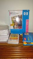 Photo showing a pack of HP Premium Plus photo paper with multiple smaller packs and loose sheets stacked around it.