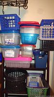Various stacked plastic storage boxes and baskets in blue, black, clear, red, and pink colors.