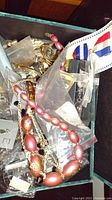 Full view of assorted costume jewelry pieces including pink bead necklace, metal chain links, and jewelry packaging.