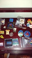 Photo showing enamel lapel pins arranged on a wooden surface including state and event logos plus corporate and souvenir pins.