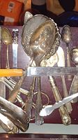 Image showing a mixed assortment of tarnished silver plate utensils including spoons and spreaders with ornate handles in a wooden box