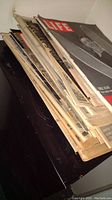 Stack of LIFE magazines and other vintage magazines stacked on black surface showing yellowed and worn edges