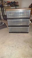 Front view showing three clear plastic drawers with black handles and the faux wood top panel.