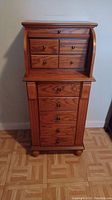 Front view of the jewelry armoire showing 4 small drawers visible, and 5 larger drawers below with wood grain and small round knobs.