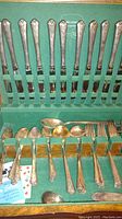 Photo of the full flatware set laid out in an original vintage green felt box; includes various forks, spoons, knives with floral patterned handles.