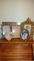 Photo showing a group of six tabletop picture frames of various designs including heart-shaped, oval, rectangular and ornate frames with vintage photographs inside.