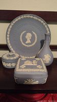 Four Wedgwood jasperware pieces displayed together: Silver Jubilee plate, square covered box, round covered box, and bud vase in blue with white relief