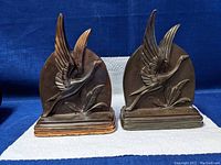 Front view of both bronze metal bird-themed bookends side by side on a blue background.