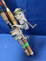 Two fishing rods bundled together showing Daiwa and Shakespeare spinning reels attached to cork handles with visible signs of wear and damage
