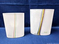 Front view of both white matte finish vases with vertical multicolor rainbow stripes showing Kosta Boda logo.