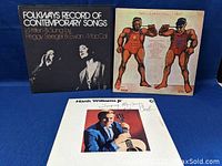 Photo showing front covers of three vinyl records: Folkways Record of Contemporary Songs by Peggy Seeger & Ewan MacColl, an album with wrestlers on the cover, and Hank Williams Jr. Singing My Songs.