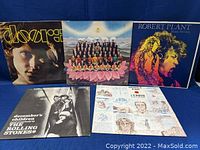 Five vintage rock vinyl records with covers visible for The Doors, The Beatles, Robert Plant, The Rolling Stones, and John Lennon.