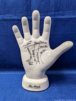 Ceramic hand figurine front view showing palmistry lines and labels on the palm, standing against a blue fabric backdrop.