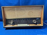 Front view of vintage Graetz Polka 113E tube radio, showing woven speaker grille, wooden cabinet, tuning and volume knobs, and push buttons.