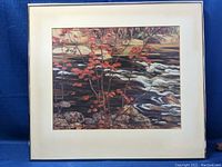 Framed print of a river scene with autumn leaves, showing the colors and details of the image clearly against a blue backdrop.