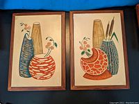 Both framed still life pottery art pieces side by side on blue background, showing full artwork and frames.