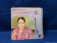 Vinyl record cover featuring M.S. Subbulakshmi in a maroon saree with a large bindi, traditional South Indian musical instrument illustration beside her.