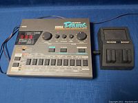Front view of Korg Super Drums DDM-110 drum machine alongside reverb boost pedal on blue surface